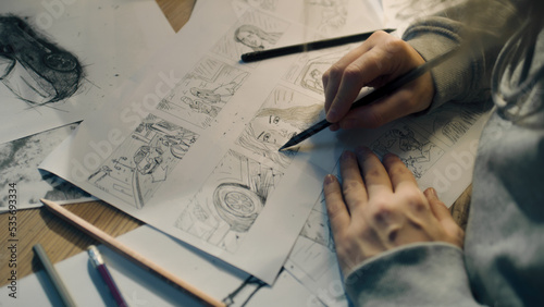 Young female artist draws sketches of comic book characters on a sheet of paper. The illustrator creates a storyboard. Storytelling concept. Video editing.