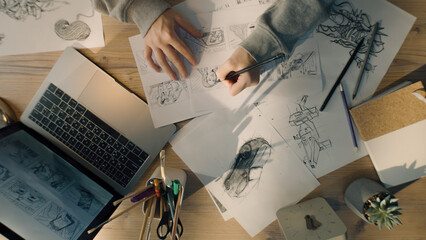 Young female illustrator drawing pencil sketches on paper. Drawings on the sheet of papers in front of her. Illustration animation, storyboard, video game film production, animation design studio.