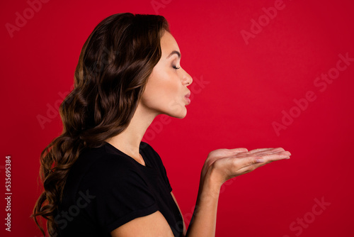 Photo of charming dreamy young woman wear black t-shirt sending kiss arms empty space isolated red color background