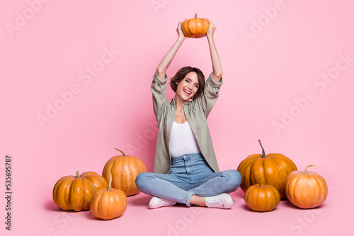 Full length portrait of satisfied glad young lady sit arms hold pumpkin above head isolated on pink color background photo