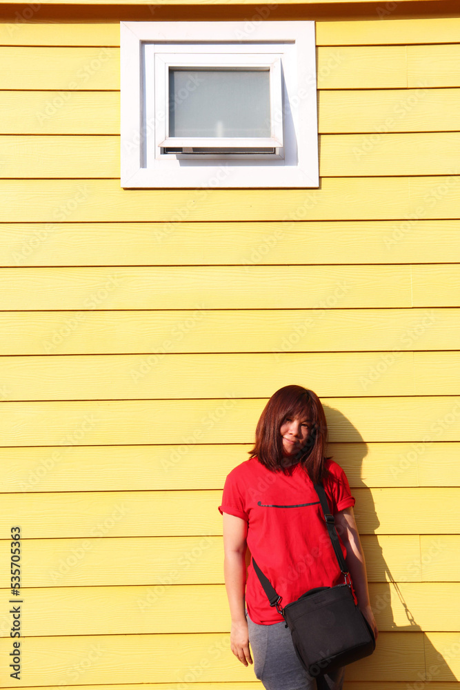 Asian woman lady looking away standing on yellow wall background. a woman wears a red t-shirt for rest time vacation, light and shadow.