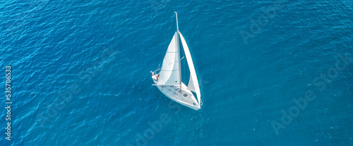 Aerial view of beautiful white sailboat sailing in the blue sea on a sunny day. Peaceful landscape with yacht. Top view of boat