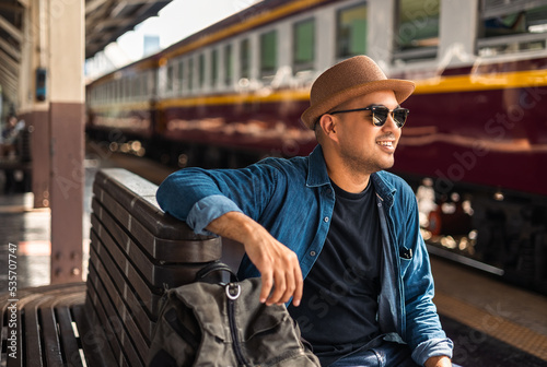 Freedom traveler young asian man at terminal train station. Happy tourist travel by train on vacation time holiday weekend trip. Male Backpacker arrival at platform railway.
