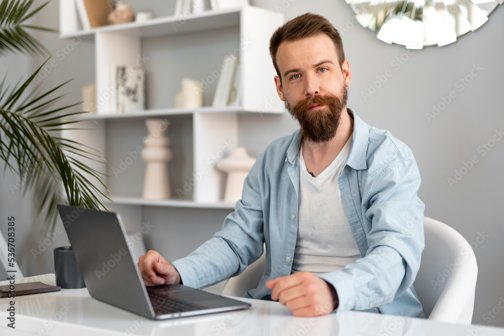 Stylish bearded man working on laptop from home sitting at the table Stylish bearded man working on laptop from home sitting at the table