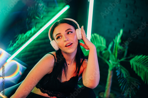 Fashion pretty woman with headphones listening to music over neon background at studio.