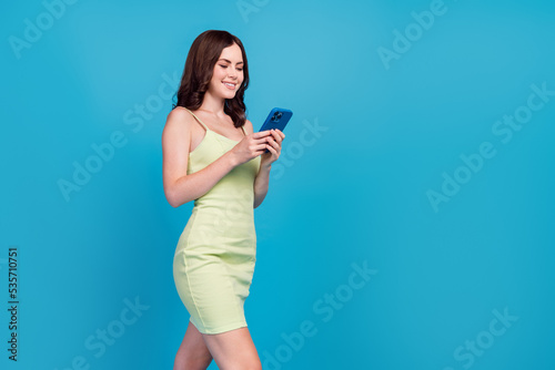 Photo of funny cute girl dressed green clothes walking communicating modern device empty space isolated blue color background
