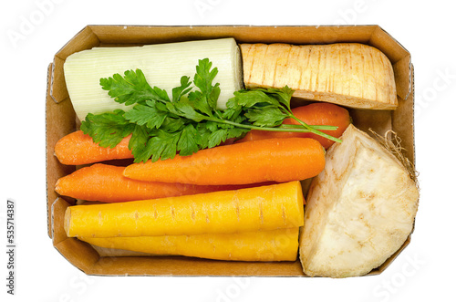 Fresh winter soup pack, uncut and prepacked, in a cardboard tray, from above, isolated over white. Orange and yellow carrots, a quarter of a celery root and of a parsnip, a piece of leek, and parsley.