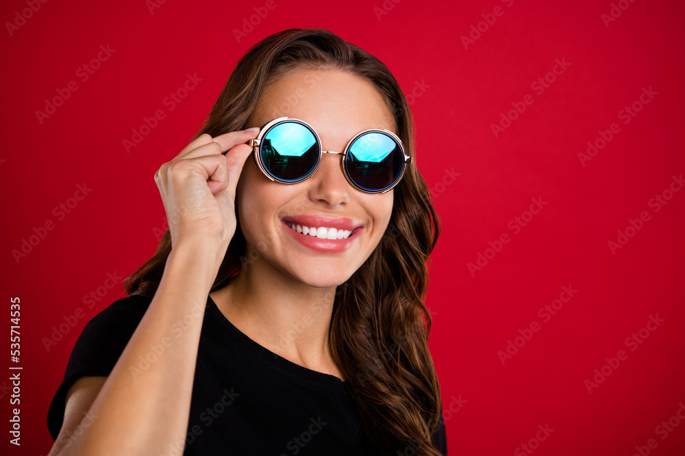 Photo of adorable charming young woman wear black t-shirt arm dark eyewear looking empty space smiling isolated red color background