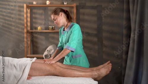 Physiotherapist massaging male patient with injured leg. Sports injury treatment. Therapist applying pressure on male leg. Hands of massage therapist massaging legs of young man in spa photo