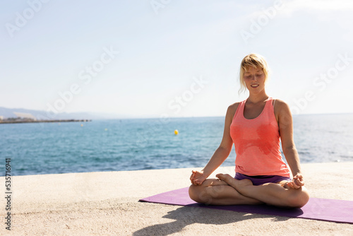  Beautiful young woman practising yoga outside. Fit woman doing stretching exercises at the beach.