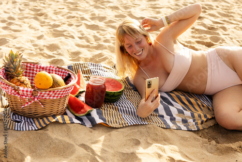 Cheerful young woman enjoy at tropical sand beach. Young woman taking a picture of fruit on the beach.. photo