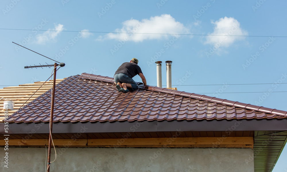 Workers install metal roofing on the wooden roof of a house. Workers install metal roofing on the wooden roof of a house.
