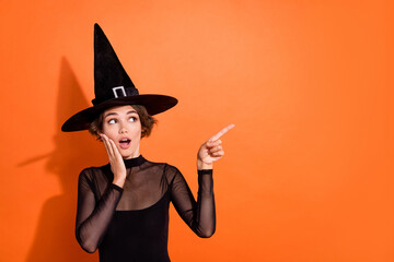 Photo of pretty young woman touch face imoressed point copyspace wear stylish black halloween witch clothes isolated on orange background