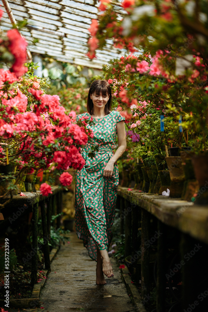 A girl in a green dress walks in a garden of azaleas of various bright colors