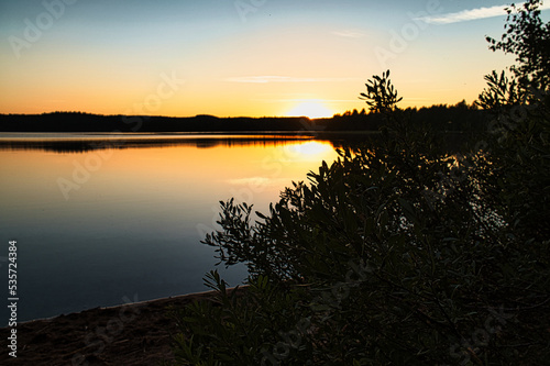 Sunset with reflection on a Swedish lake in Smalland with bushes in the foreground