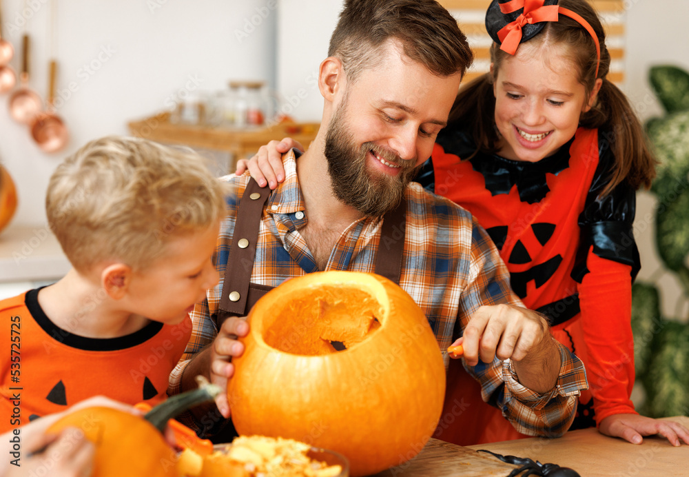 Fototapeta premium Children and dad making Jack-o-Lantern together at home, carving Halloween pumpkin