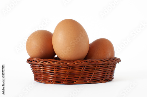 Profile view of fresh, natural brown chicken eggs in mini wicker basket. Isolated on white background with selective focus.