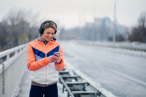 Young woman taking a break from jogging on the bridge and using smartphone