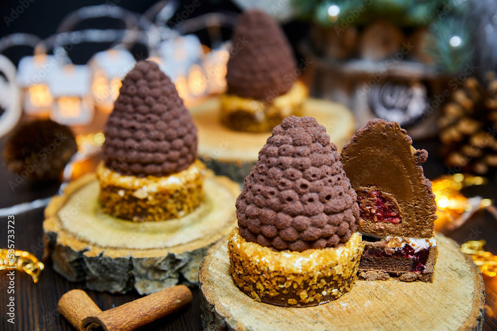 Christmas cakes in the form of fir cones from a chocolate tartlet and mousse against a background of glowing garlands Christmas cakes in the form of fir cones from a chocolate tartlet and mousse against a background of glowing garlands