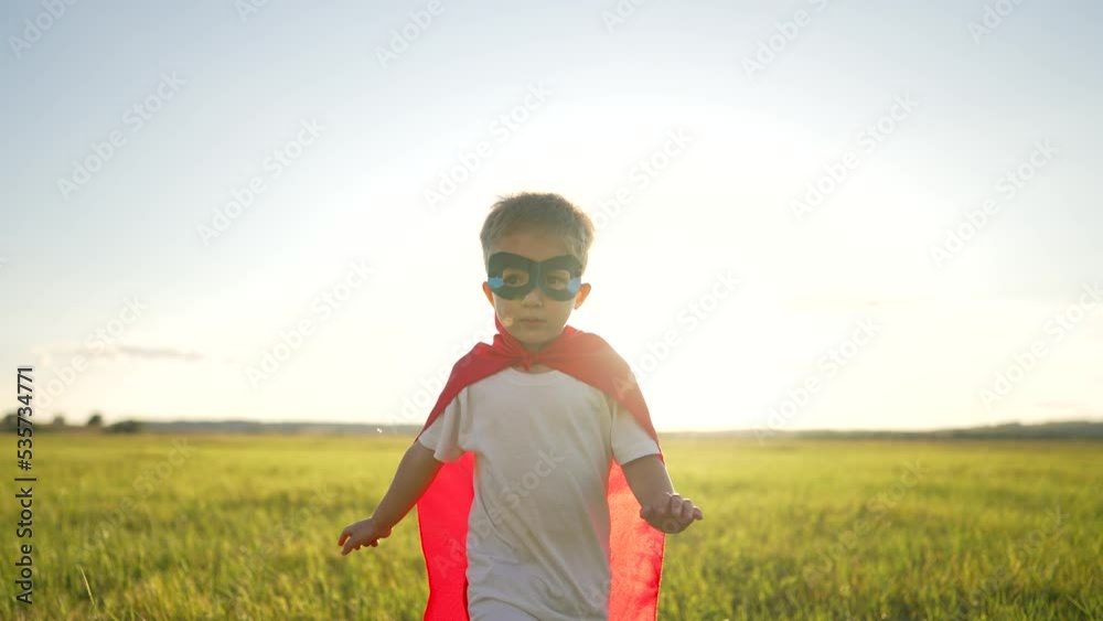 Happy child in park at sunset. Superhero winner. Boy in a red cloak and mask runs through grass.Child plays superhero in nature.Boy dressed as superhero plays in park at sunset.Childhood dream concept Happy child in park at sunset. Superhero winner. Boy in a red cloak and mask runs through grass.Child plays superhero in nature.Boy dressed as superhero plays in park at sunset.Childhood dream concept