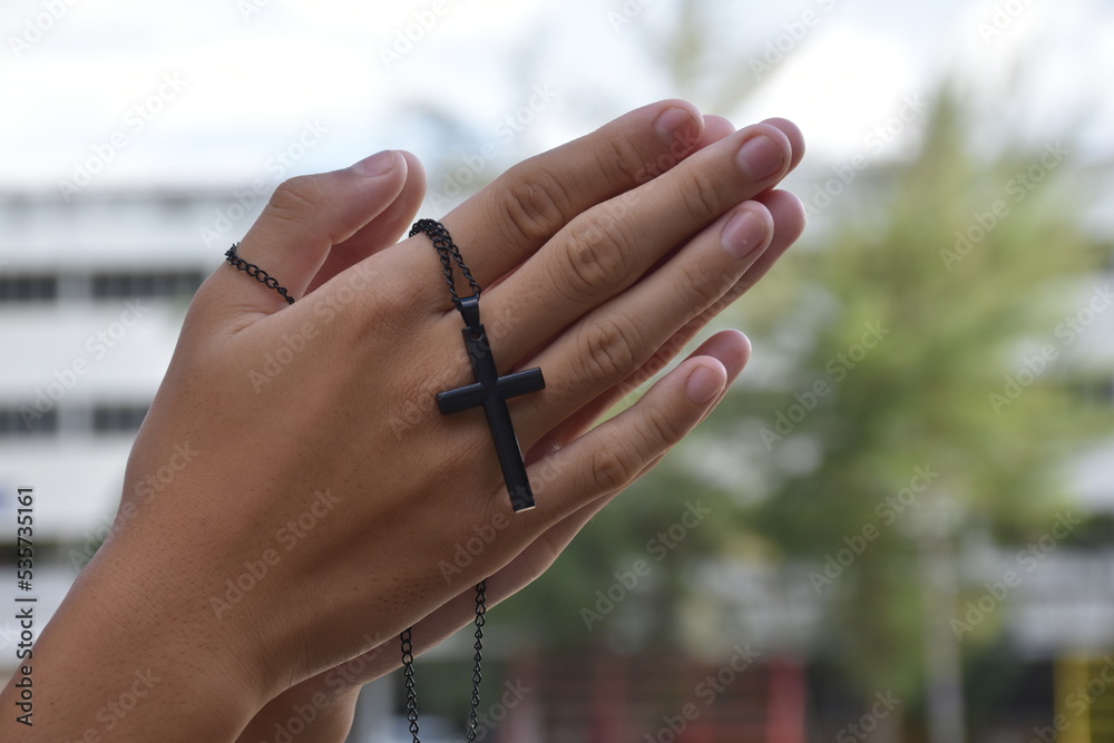 An Asian child holds a metal necklace with a cross on the top and is praying to respects to Jesus outside the church, soft and selective focus.
