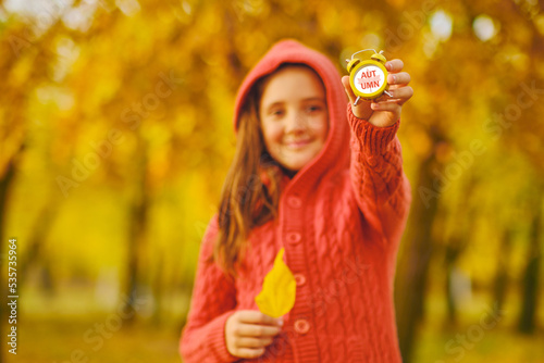 Cute kid girl holds a alarm clock in the Autumn park.