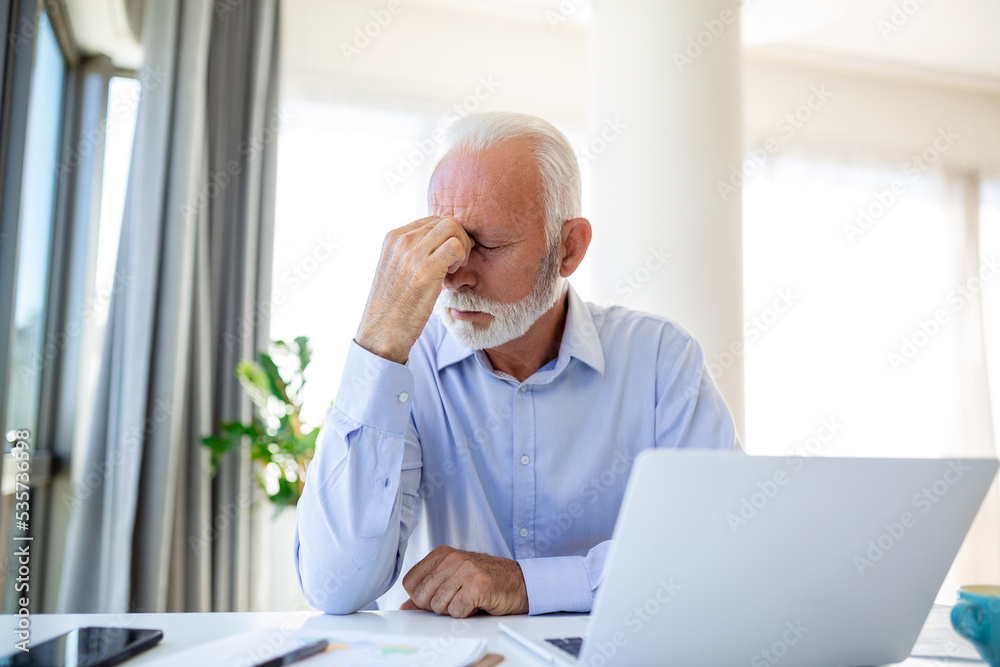 Stressed mature businessman with laptop. He could also have a headache. He is sitting in the boardroom. There are documents and laptop on the table. Copy space Stressed mature businessman with laptop. He could also have a headache. He is sitting in the boardroom. There are documents and laptop on the table. Copy space