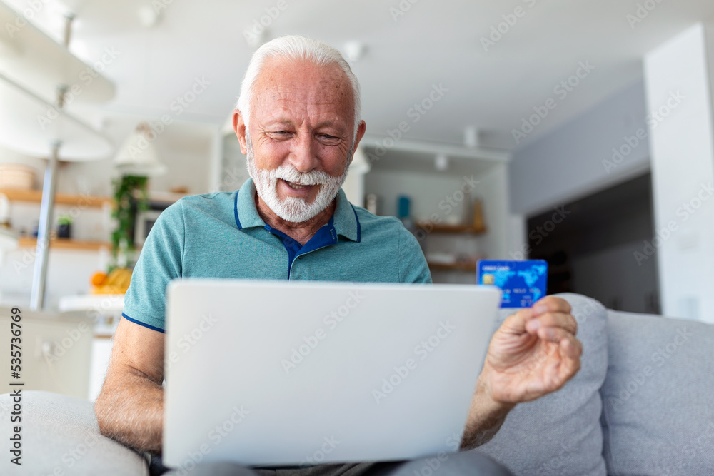Mature man using laptop, holding plastic credit or debit card, senior grey haired customer making secure internet payment, shopping or browsing online banking service, entering information Mature man using laptop, holding plastic credit or debit card, senior grey haired customer making secure internet payment, shopping or browsing online banking service, entering information