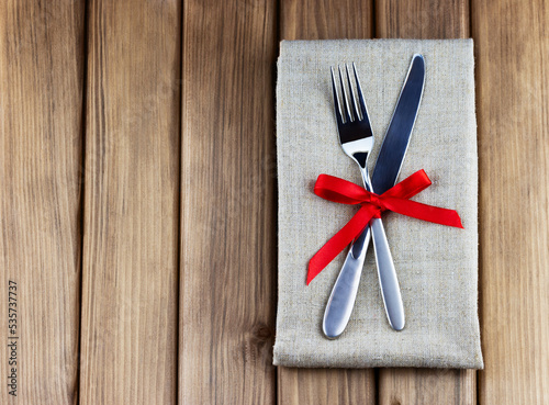 Romantic dinner concept. Top view of table appointments: napkin, silver fork and knife decorated red bow on wooden background