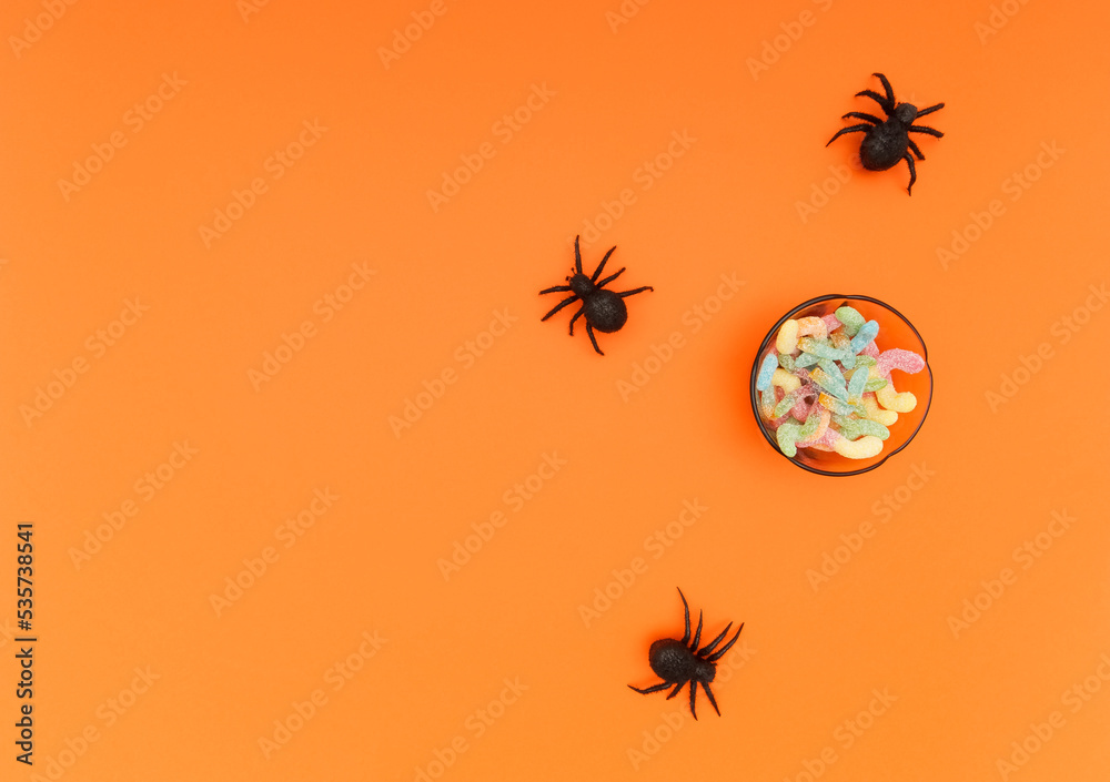 Some black spider toys and a bowl full of candy. Orange background