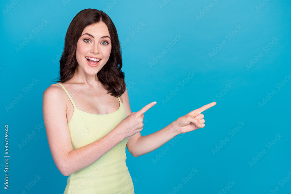 Portrait of astonished cheerful girl direct fingers empty space ad isolated on blue color background Portrait of astonished cheerful girl direct fingers empty space ad isolated on blue color background
