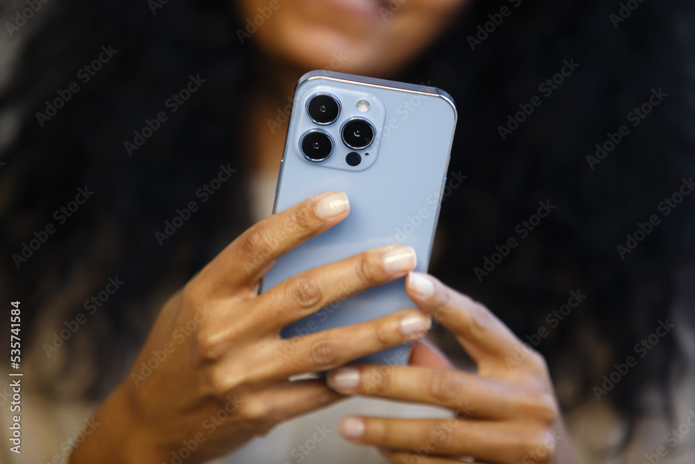 Black woman using mobile phone. African female person browsing app on modern smartphone. Download stock photo of new cellphone with triple camera Black woman using mobile phone. African female person browsing app on modern smartphone. Download stock photo of new cellphone with triple camera
