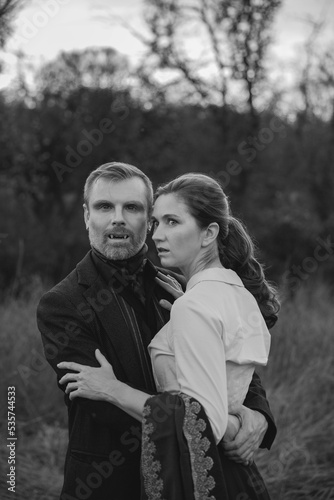 Vampire woman wearing in a burgundy coat holding lantern in autumn forest. Victorian style vintage. White and black photo