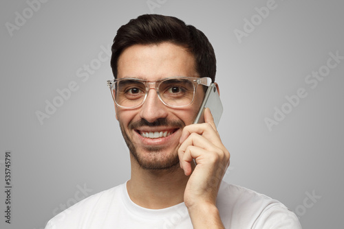 Man on gray background holding cellphone next to ear during communication smiling with confidence © Damir Khabirov