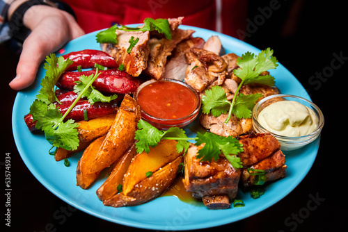 Waiter holding a large platter with Shish kebab, grilled potato and sauces. Close-up, selective focus