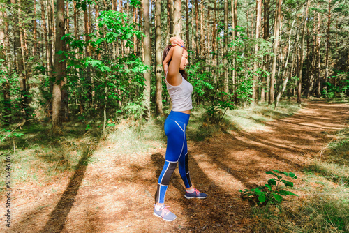 Young pretty Woman stretching arms and breathing fresh air in a summer forest while exercising. Workouts and Lifestyles concept. Healthy life and Healthcare theme.Nature and Outdoors concept.