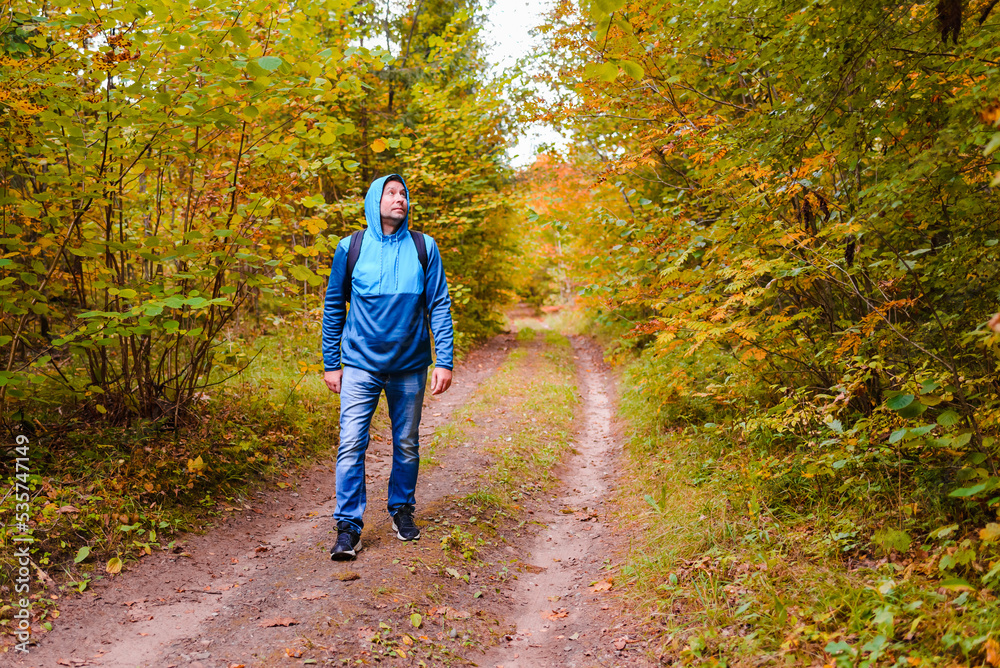 Fototapeta premium A middle age male hiking with a backpack.Man walks along the autumn forest path way.A healthy lifestyle in nature.