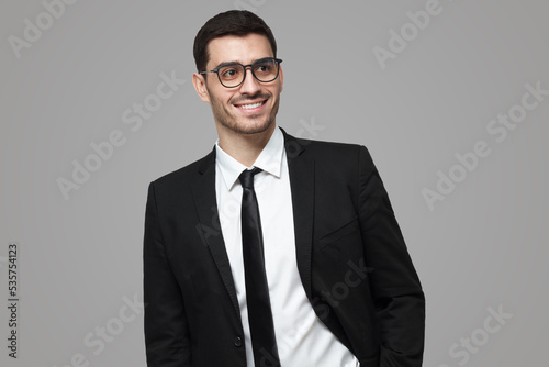 Business man in black suit looking away while standing in studio, isolated on grey background