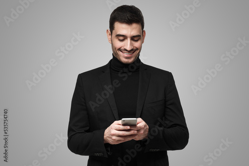 Young business man looking attentively at phone screen, browsing web pages and smiling chatting
