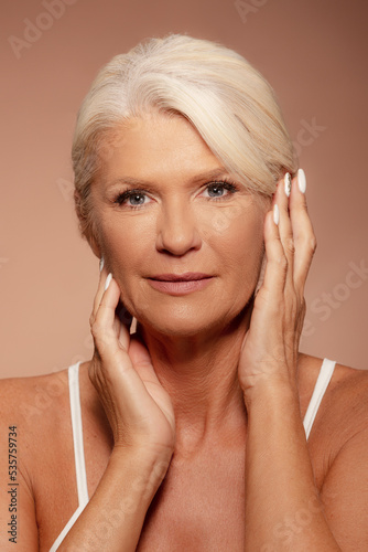 Portrait of a beautiful mature woman with beautiful skin, standing over a beige background 