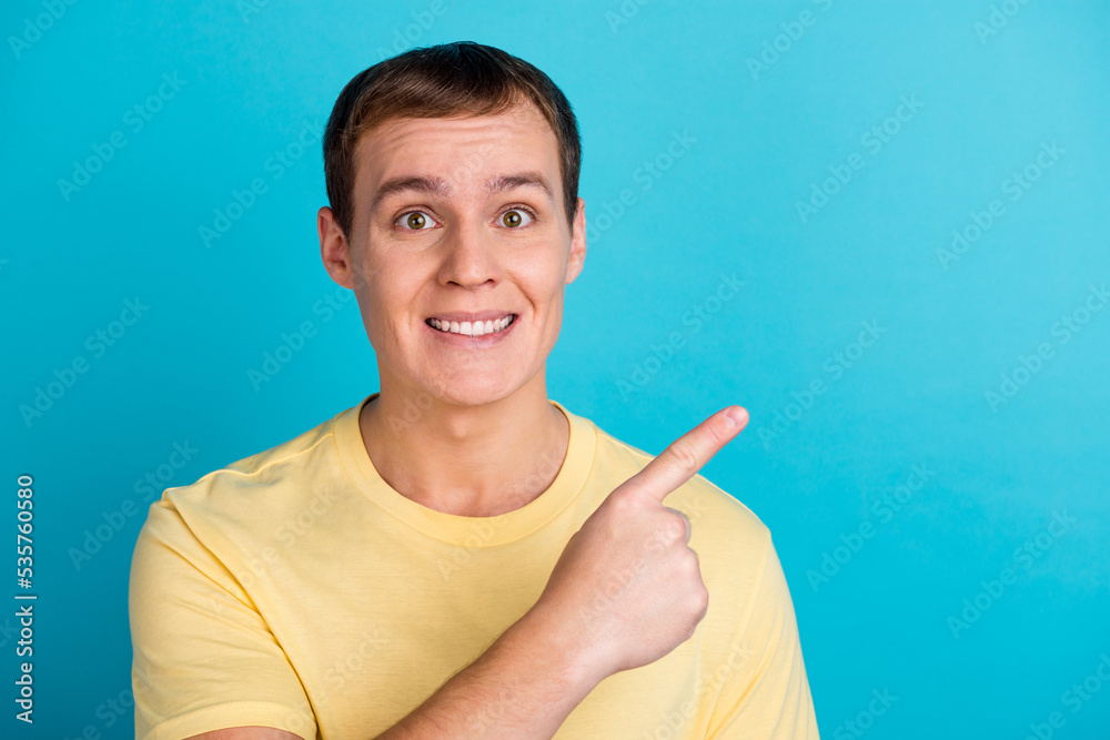 Portrait of a happy young man in t-shirt pointing fingers away copy space isolated over blue background Portrait of a happy young man in t-shirt pointing fingers away copy space isolated over blue background