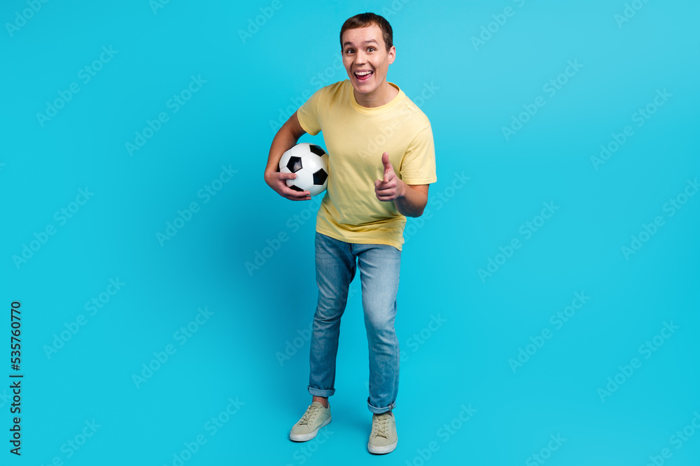 Soccer player man fan with ball pointing you hand gesture isolated on blue color background