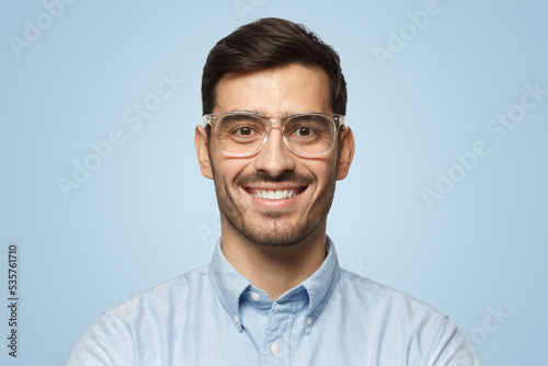 Smart businessman smiling at camera in trendy transparent glasses, isolated on blue background © Damir Khabirov