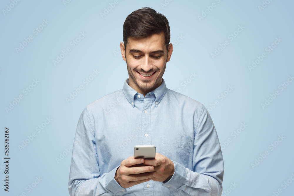 Young smiling business man in blue shirt reading sms, using phone on blue background Young smiling business man in blue shirt reading sms, using phone on blue background