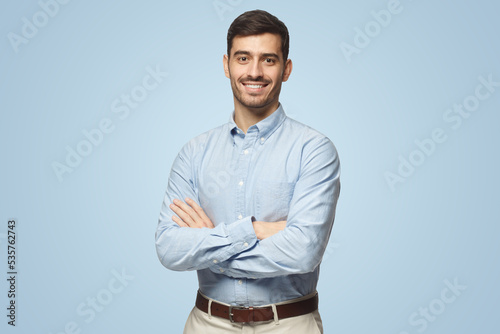 Handsome smiling business man in blue shirt standing with crossed arms on blue background