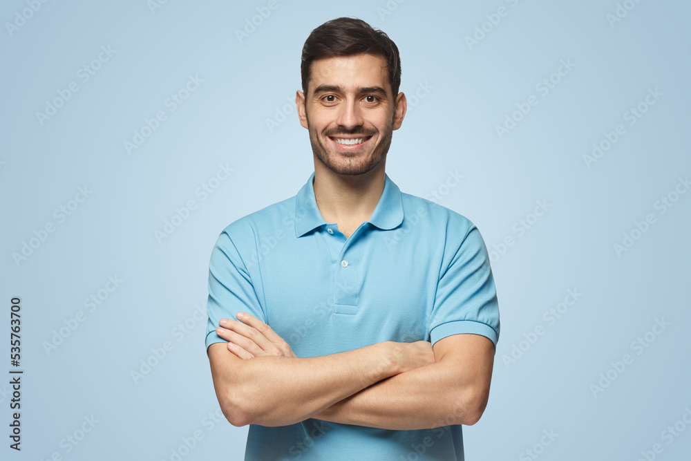 Smiling handsome man in blue polo shirt standing with crossed arms on ...