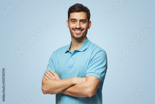 Portrait of young european man on blue background in polo shirt with crossed arms smiling at camera