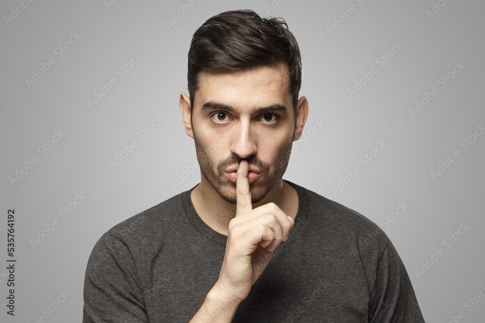 Man dressed in casual t-shirt, pressing finger to lips as if asking to keep silence Man dressed in casual t-shirt, pressing finger to lips as if asking to keep silence
