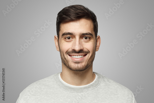 Closeup headshot of young smiling European male isolated on gray background