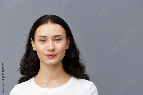 a gentle woman stands on a dark background in a tight white T-shirt  calmly lowered her hands down and looks forward